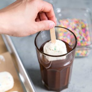 The image features a hand dipping a stick of ice cream into a glass full of cocoa dip