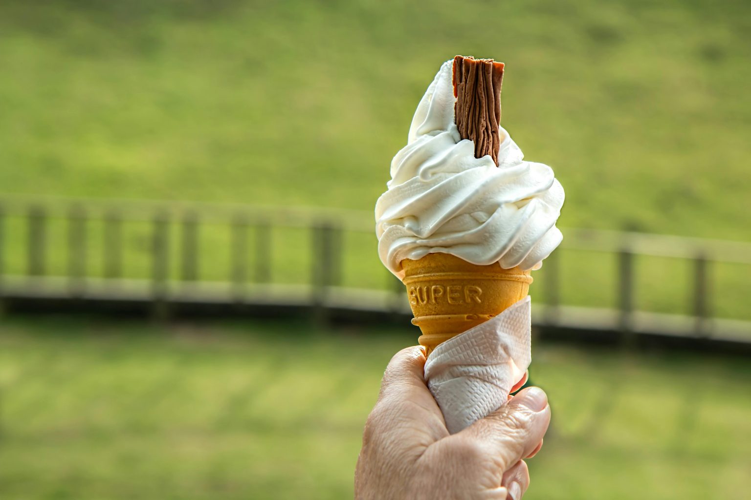 The image shows a hand holding an ice cream cone full of ice cream