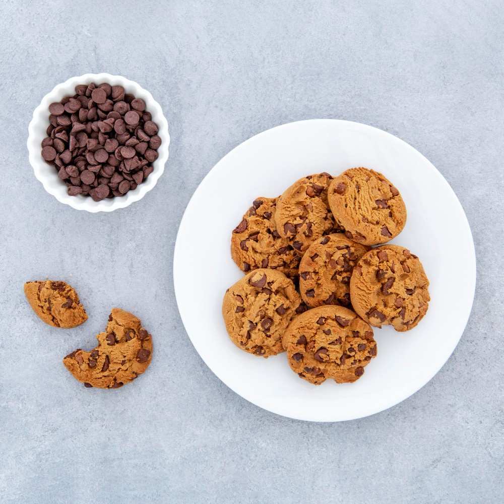 The image displays a plate full of chocolate chip cookie alongside a bowl full of choco chips.