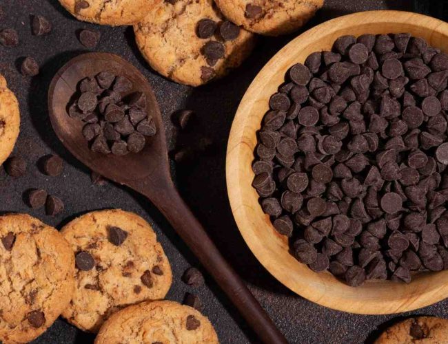 The image features a pan and spatula full of choco chips surrounded by choc chip buiscuits.